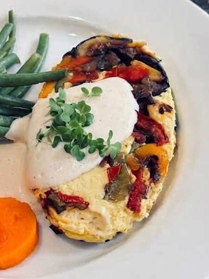 Slice of Mediterranean crustless tofu quiche with roasted peppers, aubergine and courgette, topped with creamy vegan dressing and microgreens.